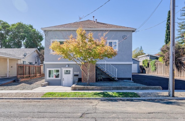 view of front facade with an outbuilding, stucco siding, stairs, and fence