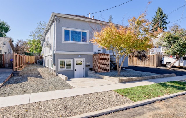 view of front of house with stucco siding, stairs, and fence