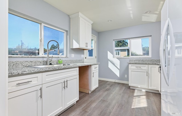 kitchen featuring light wood finished floors, light stone countertops, freestanding refrigerator, white cabinets, and a sink