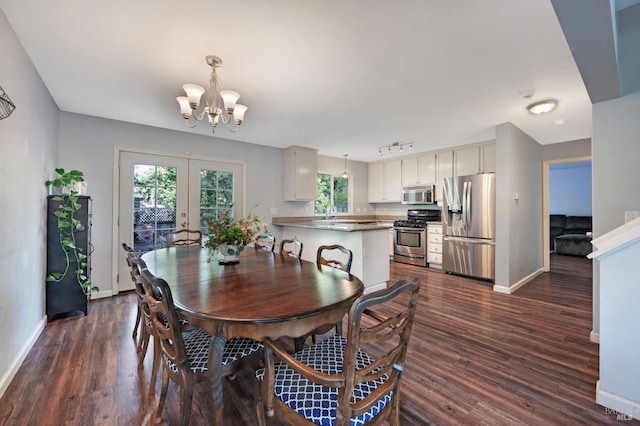 dining space with a chandelier, dark wood-style floors, rail lighting, and baseboards