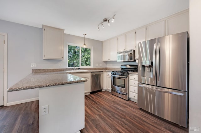 kitchen featuring appliances with stainless steel finishes, dark wood-type flooring, a peninsula, and a sink