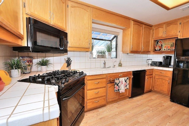 kitchen featuring visible vents, black appliances, light wood-style flooring, a sink, and tile countertops