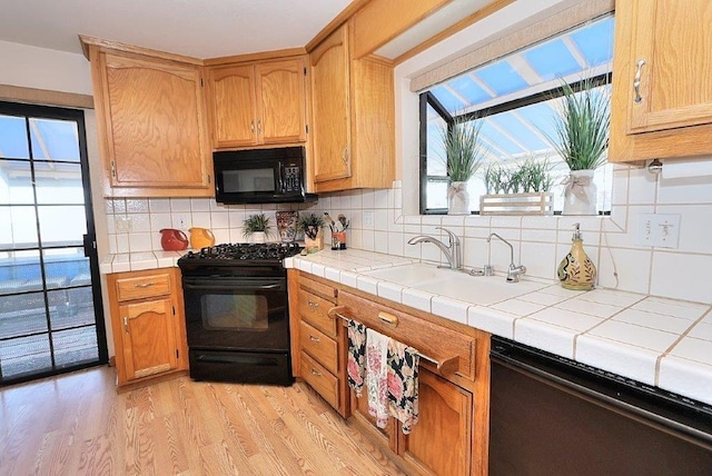 kitchen with black appliances, a sink, tasteful backsplash, tile countertops, and light wood finished floors