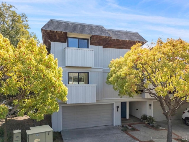 contemporary home featuring a garage, a balcony, concrete driveway, and a shingled roof