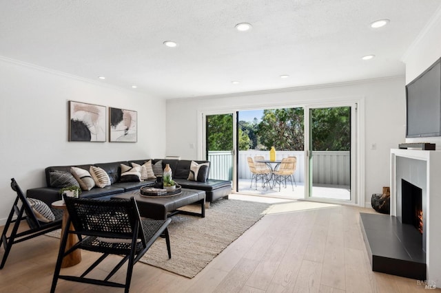 living room featuring a textured ceiling, recessed lighting, a lit fireplace, crown molding, and light wood finished floors