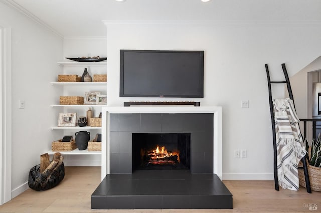 interior details featuring a tiled fireplace, crown molding, wood finished floors, and baseboards