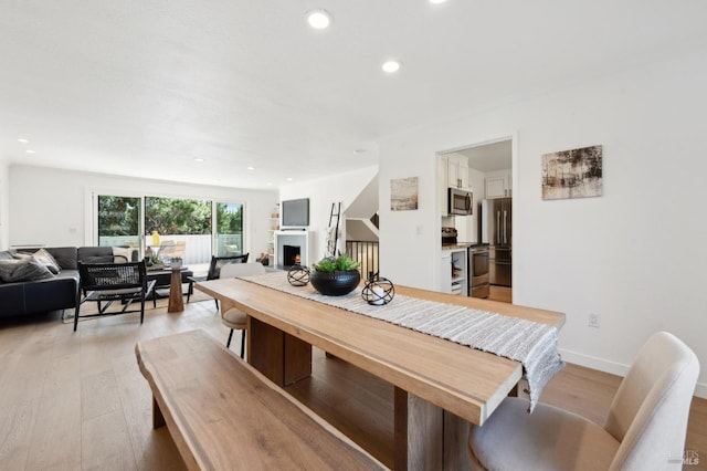 dining space featuring recessed lighting, baseboards, a lit fireplace, and light wood-style flooring