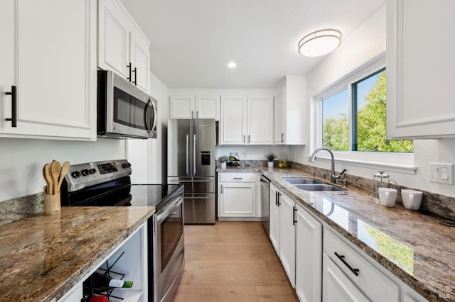 kitchen featuring light wood finished floors, white cabinets, stainless steel appliances, and a sink