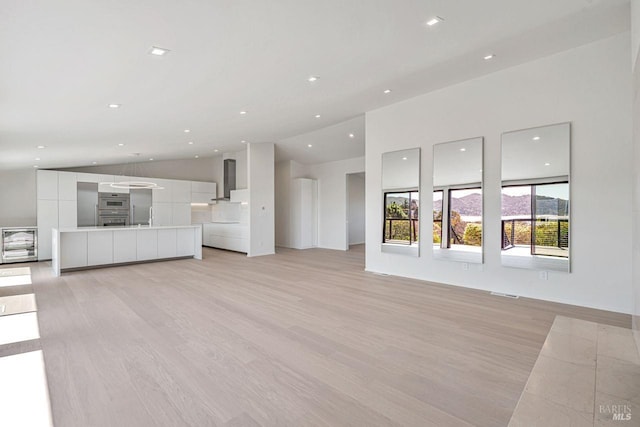 unfurnished living room with recessed lighting, lofted ceiling, and light wood-style flooring