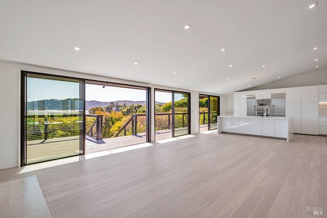 unfurnished living room featuring recessed lighting, a mountain view, lofted ceiling, and light wood-style floors