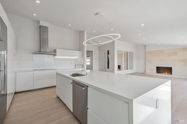 kitchen featuring a sink, white cabinets, stainless steel dishwasher, wall chimney range hood, and modern cabinets