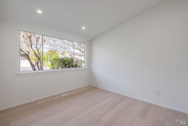 spare room with light wood-type flooring, visible vents, and baseboards