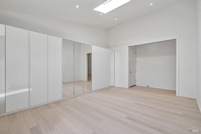 unfurnished bedroom with recessed lighting, a skylight, light wood-type flooring, and a towering ceiling