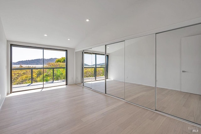 unfurnished bedroom featuring a mountain view, light wood-style floors, access to exterior, and vaulted ceiling