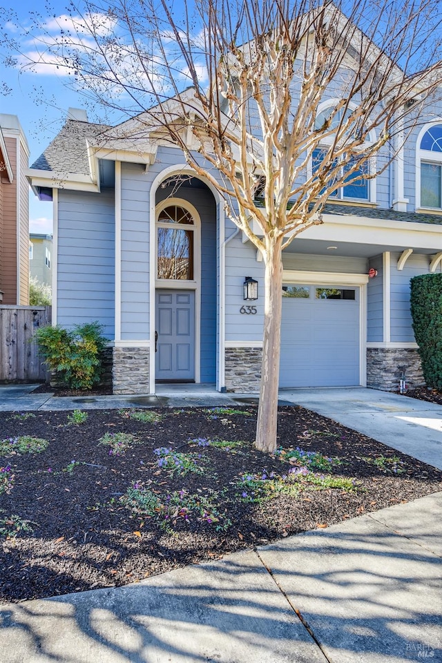 entrance to property with a porch, fence, driveway, stone siding, and an attached garage