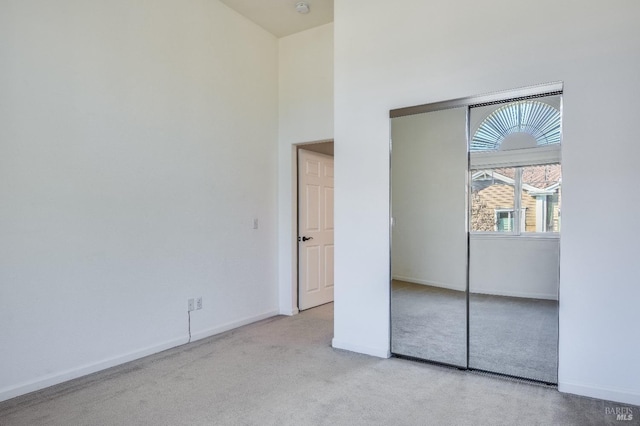 unfurnished bedroom with baseboards, carpet floors, a closet, and a towering ceiling