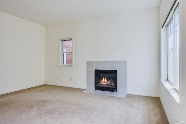 unfurnished living room with a tiled fireplace, baseboards, carpet floors, and plenty of natural light
