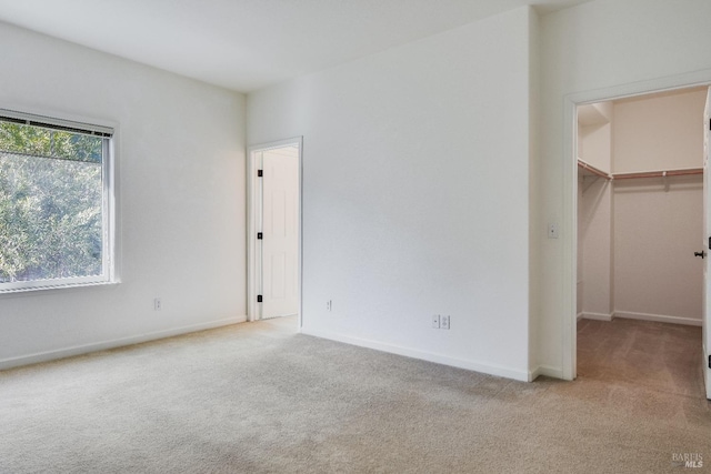 unfurnished bedroom with a spacious closet, a closet, carpet flooring, and baseboards