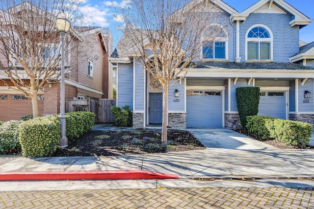 view of front of property featuring driveway, stone siding, an attached garage, and fence