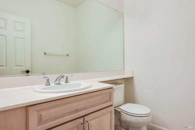 half bathroom featuring toilet, vanity, and baseboards