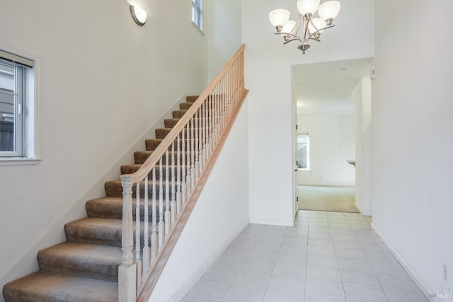 staircase with an inviting chandelier, a towering ceiling, plenty of natural light, and tile patterned flooring