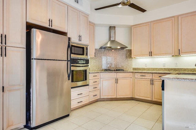 kitchen with light brown cabinetry, appliances with stainless steel finishes, wall chimney range hood, backsplash, and ceiling fan