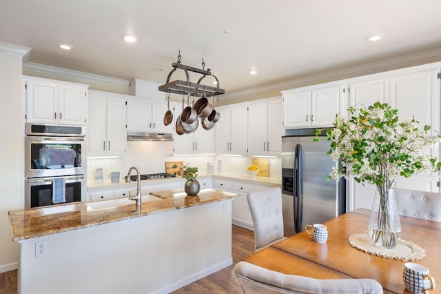 kitchen with a center island with sink, under cabinet range hood, backsplash, stainless steel appliances, and white cabinets