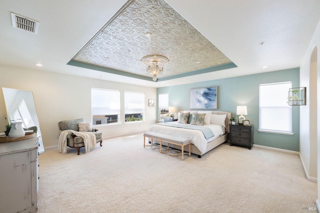 carpeted bedroom with a tray ceiling, baseboards, and visible vents