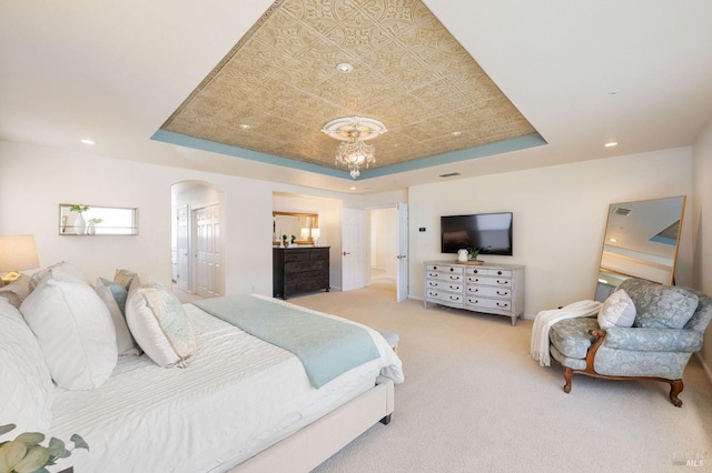 carpeted bedroom featuring ensuite bathroom, a tray ceiling, recessed lighting, arched walkways, and an inviting chandelier