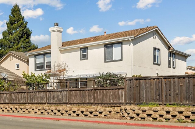 view of side of home featuring a tile roof, fence, and stucco siding