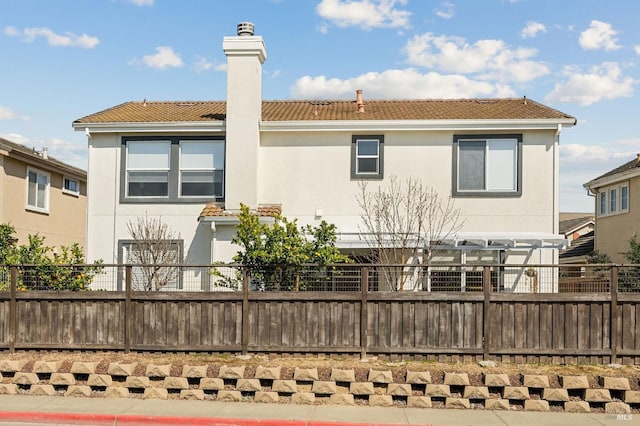 rear view of property with a tiled roof, fence, a chimney, and stucco siding