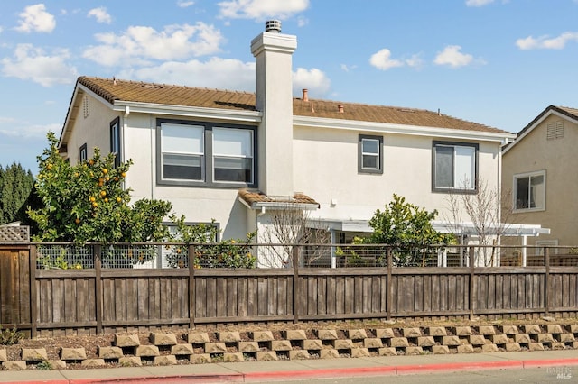 rear view of house featuring stucco siding, a tile roof, a chimney, and fence