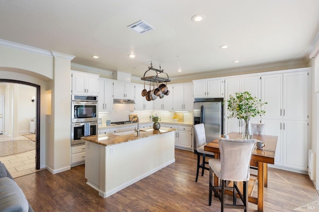 kitchen featuring visible vents, under cabinet range hood, dark wood-style floors, arched walkways, and appliances with stainless steel finishes