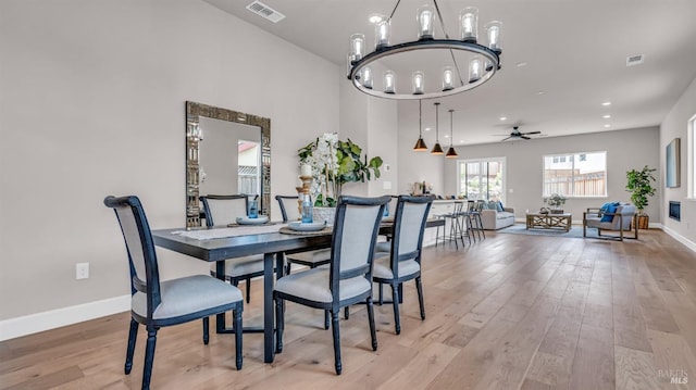 dining space featuring visible vents, ceiling fan with notable chandelier, baseboards, and light wood-style floors