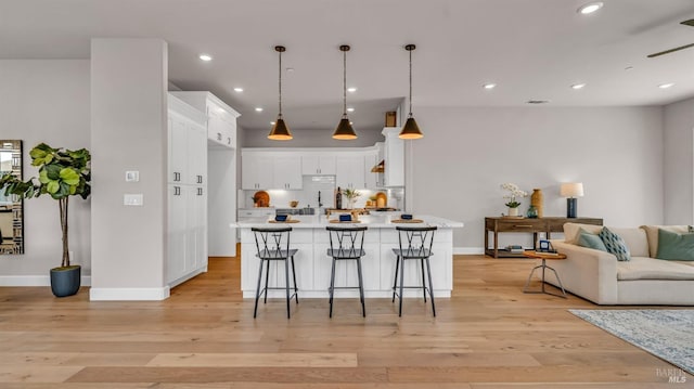 kitchen featuring light wood finished floors, open floor plan, light countertops, a kitchen breakfast bar, and white cabinets