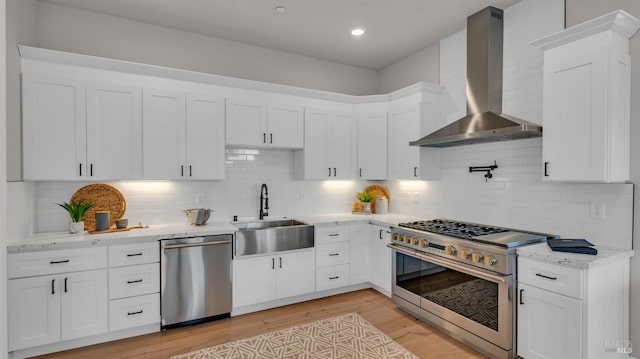 kitchen with light wood-type flooring, stainless steel appliances, white cabinetry, wall chimney exhaust hood, and a sink