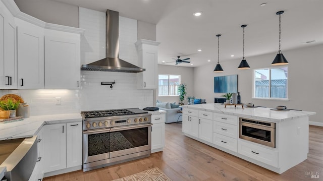 kitchen with light wood-style flooring, appliances with stainless steel finishes, wall chimney exhaust hood, and ceiling fan