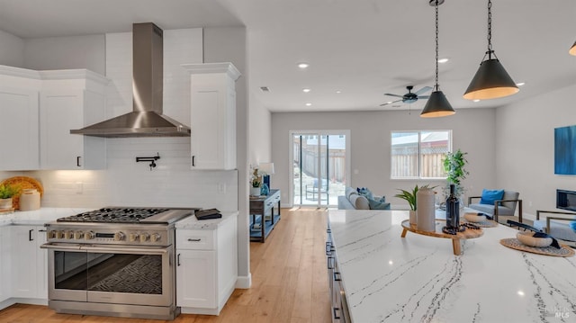 kitchen featuring open floor plan, white cabinetry, wall chimney exhaust hood, and high end stainless steel range