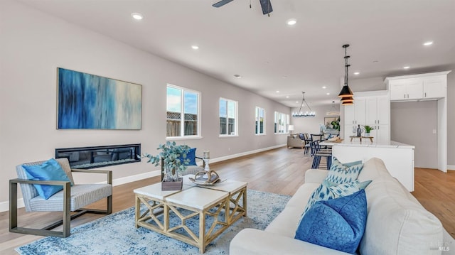 living room featuring recessed lighting, baseboards, light wood-style floors, and ceiling fan with notable chandelier