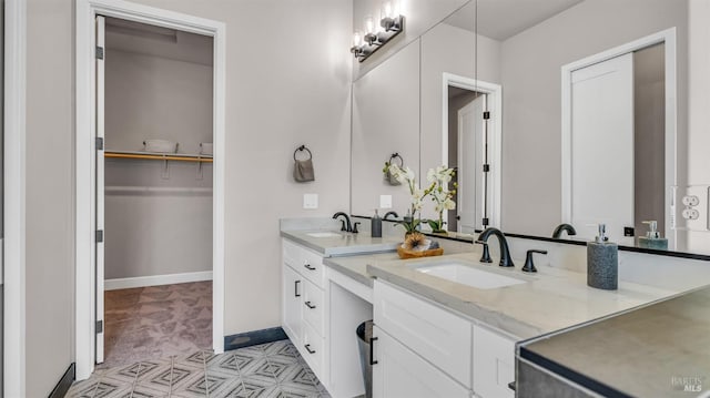 bathroom with double vanity, a walk in closet, baseboards, and a sink