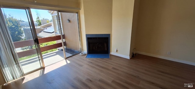 unfurnished living room featuring plenty of natural light, a tiled fireplace, baseboards, and wood finished floors