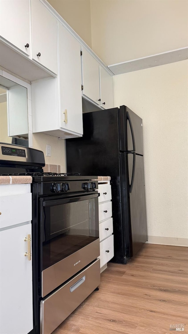 kitchen featuring white cabinets, light wood-style floors, stainless steel range with gas stovetop, and baseboards