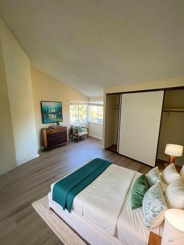 bedroom featuring a closet, a textured ceiling, wood finished floors, and lofted ceiling