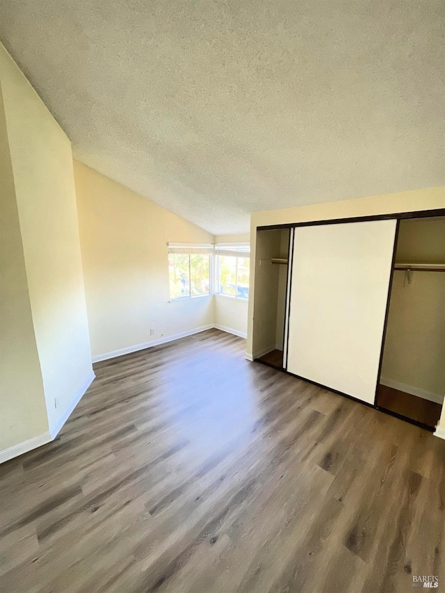 unfurnished bedroom with baseboards, lofted ceiling, a textured ceiling, and wood finished floors