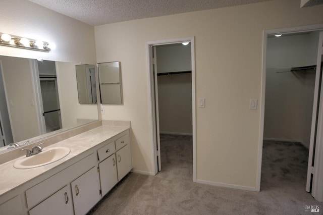 full bath with a walk in closet, vanity, and a textured ceiling