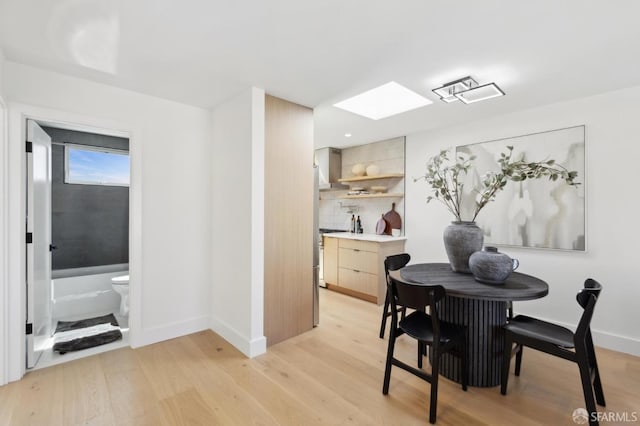 dining area featuring a skylight, baseboards, and light wood-type flooring