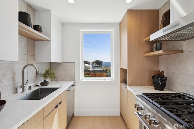 kitchen featuring open shelves, a sink, stainless steel appliances, wall chimney range hood, and light stone countertops