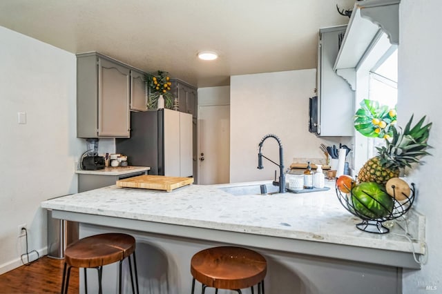 kitchen featuring a kitchen bar, gray cabinets, dark wood finished floors, freestanding refrigerator, and a peninsula