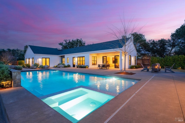 pool at dusk featuring an in ground hot tub, a fire pit, an outdoor pool, and a patio