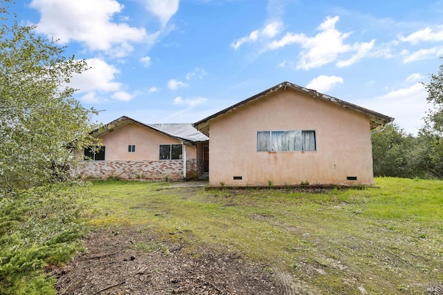 rear view of house with crawl space, stucco siding, and a lawn